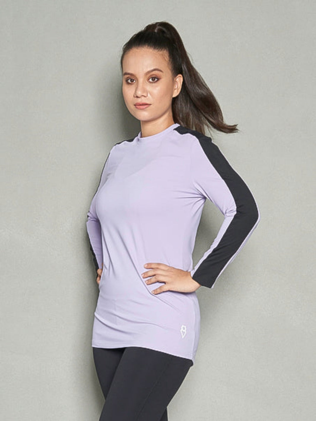 A shot of upper half of the body of a woman wearing purple long sleeve workout top with her hands on her hips.