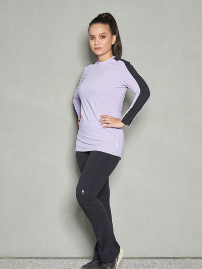 A shot of a woman wearing purple long sleeve workout top and bootleg workout pants with her hands on her hips.