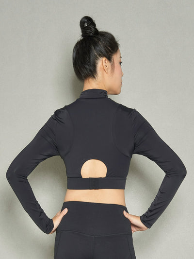 A woman with her back facing the camera while wearing a long sleeve black sports bra and black leggings with both hands on her hips.