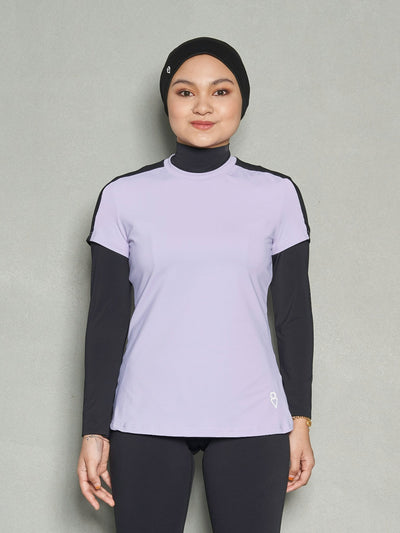 A woman standing straight facing the camera while wearing bandana sports hijab, short sleeve workout top, long sleeve black sports bra and black leggings.